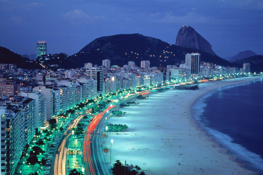 Copacabana beach at dusk with flickering building lights and sugarloaf mountain in the distance