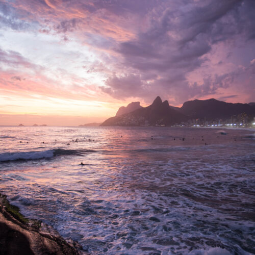 A sunset with pastel orange, yellow, and purple colors above Dois Irmãos and Pedra da Gavea from Arpoador