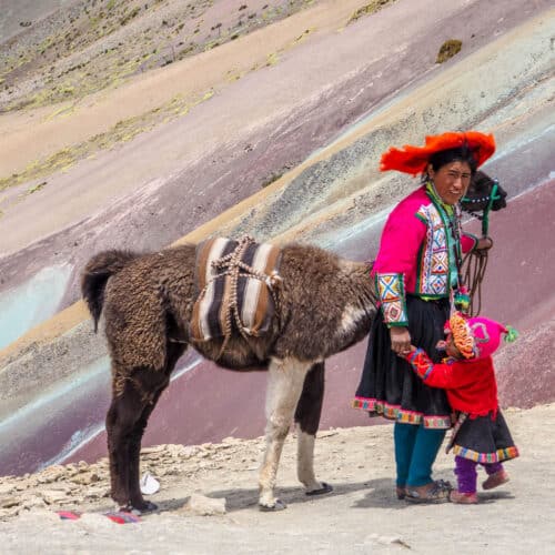 A woman with a llama and her child in front of Vinicunca Mountain in Peru