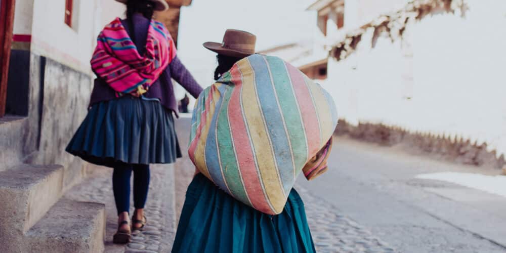 A close up view of two Peruvian women dressed in traditional attire walking down a cobblestone street