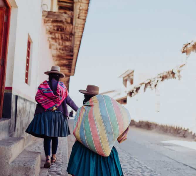 Two Peruvian women dressed in traditional attire walking down a cobblestone street