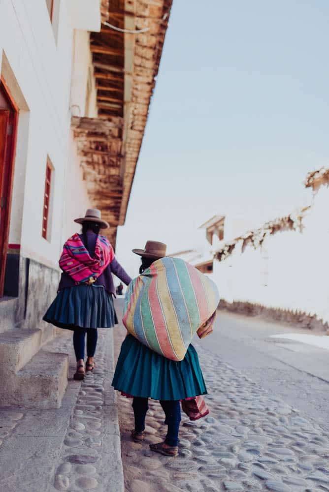 Two Peruvian women dressed in traditional attire walking down a cobblestone street